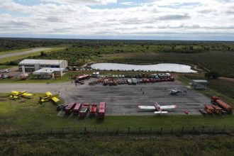 Vista aérea de uma base de combate a incêndios florestais, com aviões, caminhões e equipes de emergência preparados para atuar.