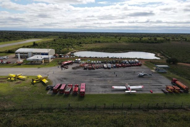 Vista aérea de uma base de combate a incêndios florestais, com aviões, caminhões e equipes de emergência preparados para atuar.
