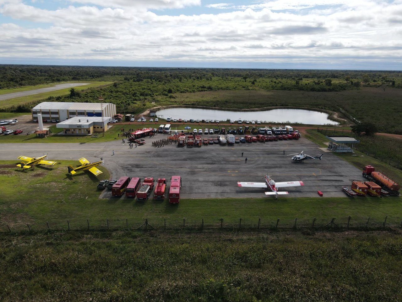 Vista aérea de uma base de combate a incêndios florestais, com aviões, caminhões e equipes de emergência preparados para atuar.