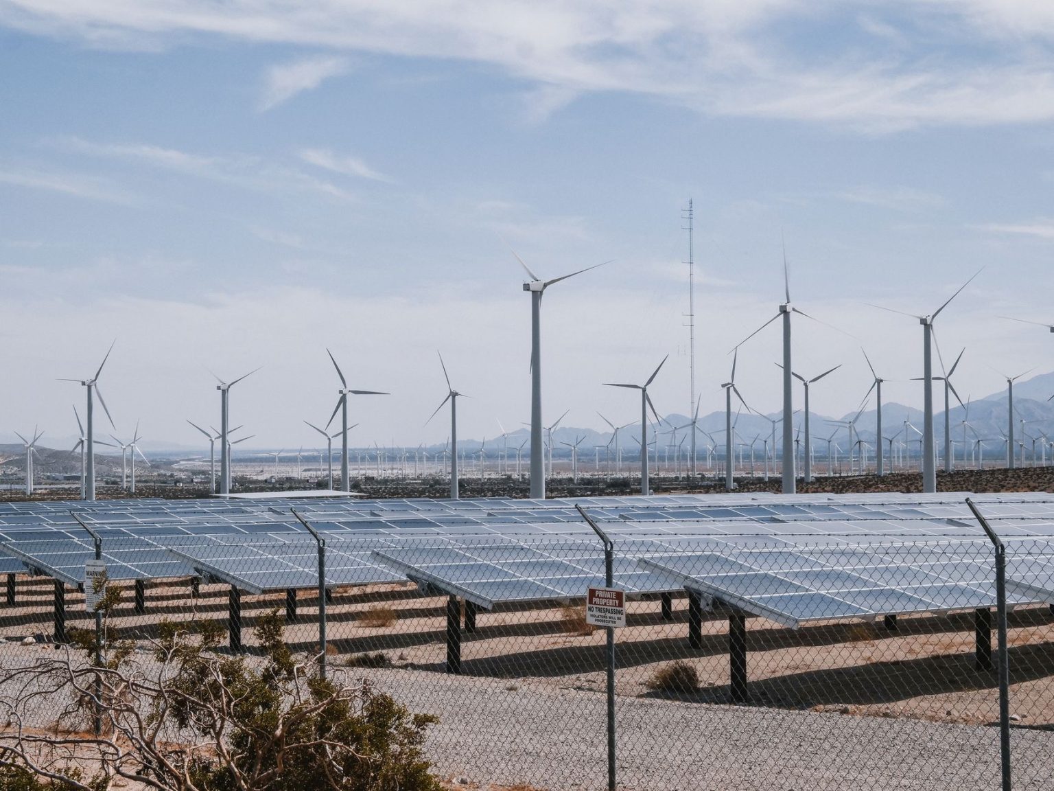 Parque de geração renovável com turbinas eólicas e painéis solares sob céu claro.