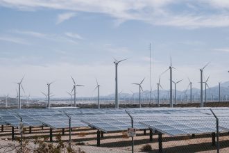 Parque de geração renovável com turbinas eólicas e painéis solares sob céu claro.