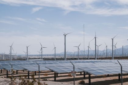 Parque de geração renovável com turbinas eólicas e painéis solares sob céu claro.