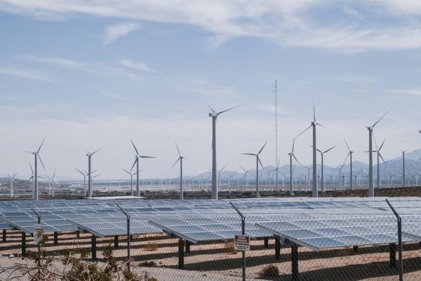 Parque de geração renovável com turbinas eólicas e painéis solares sob céu claro.