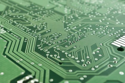 Close de uma placa de circuito impresso com chip, trilhas e componentes eletrônicos.