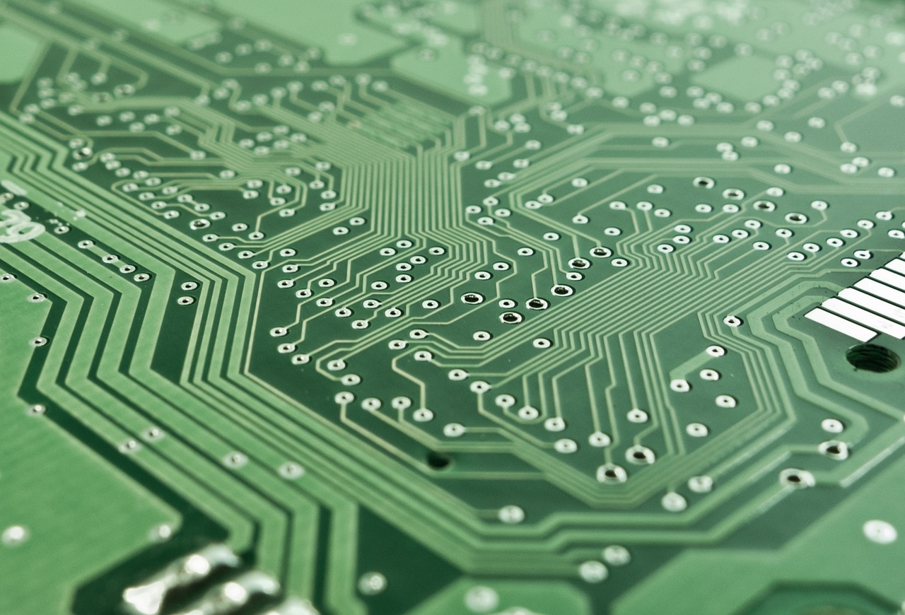 Close de uma placa de circuito impresso com chip, trilhas e componentes eletrônicos.
